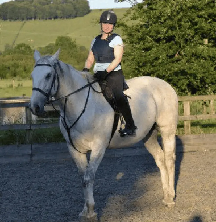 Photo of Paws2Rescue team member Yvonne sitting on top of a white horse